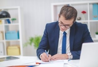 Professional man signing documents at desk – representing NRIWAY’s reliable and expert document verification services for NRIs.